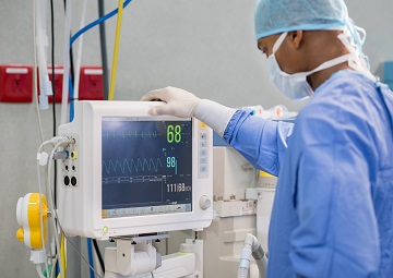 African surgeon keeping track of vital functions of the body during cardiac surgery. Surgeon looking at medical monitor during surgery. Doctor checking monitor for patient health status.